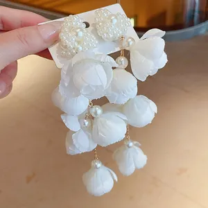 Detailed view of elegant white fabric flower and pearl heart dangle earrings.
