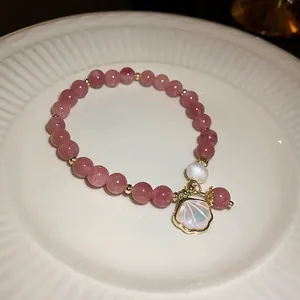 Elegant strawberry quartz bead bracelet with pearl and iridescent shell charm on a plate