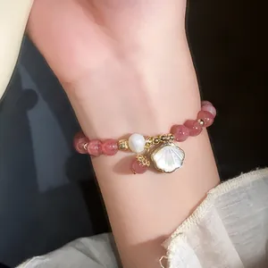 Elegant strawberry crystal beaded bracelet with pearl and shell charm detail on wrist.
