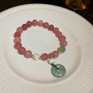 Detail view of a pink strawberry quartz beaded bracelet with pearls and green stone charm.