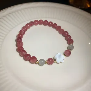 Detailed view of a pink strawberry crystal bead bracelet with a white shell flower charm