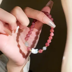 Detail view of a strawberry quartz beaded bracelet featuring a white shell cat charm