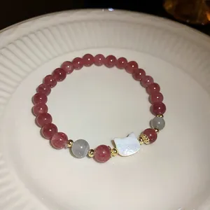 Detailed close-up of a strawberry quartz beaded bracelet with a white shell cat charm