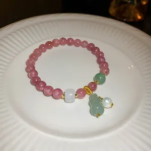 Detailed view of pink strawberry crystal bracelet with green gourd and pearl pendants.