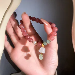 Strawberry quartz beaded bracelet featuring flower and gourd pendants held in hand