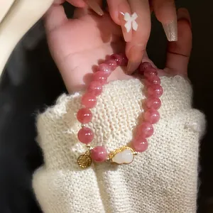 Close-up of strawberry quartz beaded bracelet with white shell gourd and gold charm.