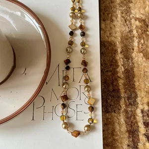 Detailed macro view of irregular tiger eye and pearl beaded necklace on a white card