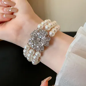 Detailansicht eines dreireihigen Perlenarmbands mit einem funkelnden Strassblumen-Anhänger.