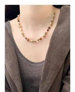 Close-up detail of an irregular tiger eye and pearl beaded necklace worn by a model