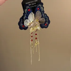Close-up of retro butterfly earrings with dark blue embroidery and gold chains