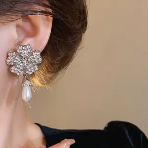 Detailansicht eleganter silberner Blumenohrringe mit Strass und Perle am Ohr des Models