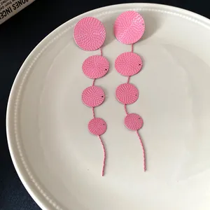 Macro view of pink long drop earrings with textured circular discs on a ceramic plate