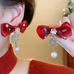 Close-up of red bow earrings with snowflake charms and white pearl drops for Christmas.
