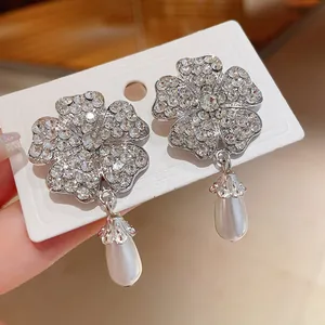 Detaillierte Nahaufnahme von silbernen Blumenohrringen mit Strass und Perlenanhängern.