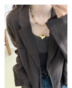 Detail of layered jewelry with heart pendant and Tiger's Eye beaded necklace on a model.