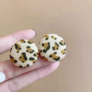 Primer plano detallado de pendientes redondos de tela con estampado de leopardo vintage.
