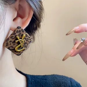 Detalle de pendientes de botón cuadrados con estampado de leopardo y logo dorado