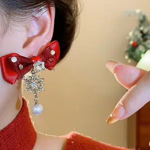 Close-up of a festive red bow earring with snowflake charm and pearl drop worn on an ear