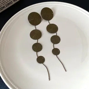 Macro view of vintage dark olive green textured disk tassel earrings on white ceramic plate