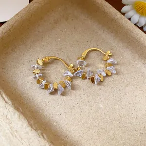 Dettaglio di orecchini a cerchio placcati oro 18k con pietre in cristallo.