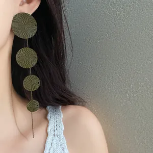 Detailed macro view of vintage green textured disk tassel earrings worn by an elegant model