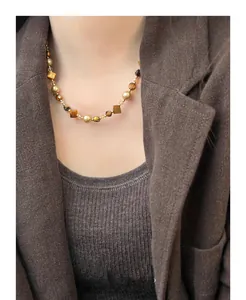 Detail of tiger eye and pearl beaded necklace on model with brown blazer style.