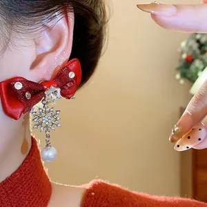 Close-up of red ribbon bow earring featuring snowflake charm and white pearl drop