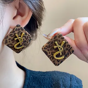 Detalle de pendientes vintage con estampado de leopardo y un gran logo dorado