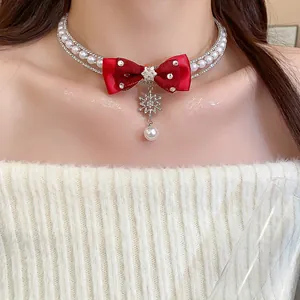 Close-up of elegant pearl choker necklace featuring a red satin bow and snowflake pendant
