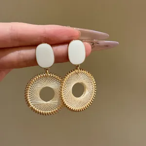 Close-up view of vintage gold woven circular drop earrings with white enamel studs