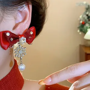 Close-up of elegant red bow earring with sparkling snowflake tassel and pearl drop