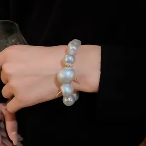 Elegant baroque pearl bracelet with gold hardware worn on wrist against dark background