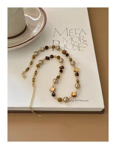 Detailed view of an irregular tiger eye and gold pearl beaded necklace on a white book.