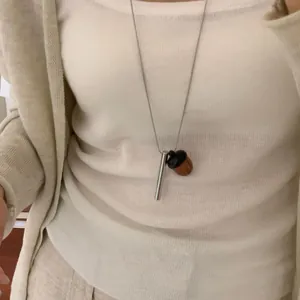 Vue détaillée d'un collier avec pendentif gland et barre argentée sur un haut crème.