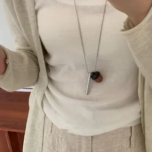 Gros plan d'un collier long avec un cylindre argenté et un pendentif gland en bois
