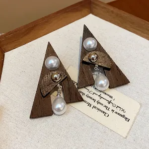 Primo piano di orecchini etnici in legno triangolari con perle a goccia pendenti