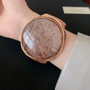 Detalle de un brazalete redondo de resina con tejido de alambre en color oro rosa