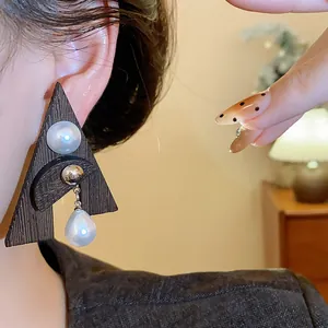 Primo piano di un orecchino a triangolo in legno con perle bianche a goccia.