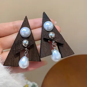 Primo piano di orecchini etnici in legno a triangolo con eleganti perle a goccia.