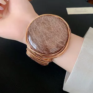 Vista detallada de un brazalete abierto de resina y alambre dorado tejido en la muñeca