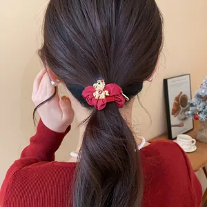 Détail d'un chouchou rouge avec un charm de cheval doré porté en queue de cheval