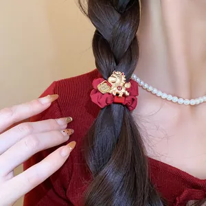 Gros plan d'un chouchou en tissu rouge avec un charm de cheval doré sur une tresse