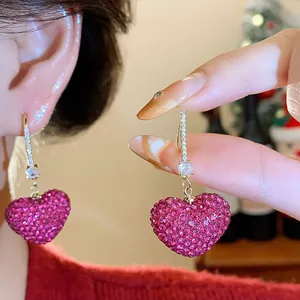 Macro close-up view of luxury pink crystal pave heart earring held by hand showing details