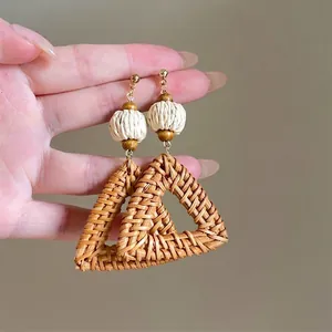 Close-up of handmade brown rattan woven triangle earrings with white textured beads