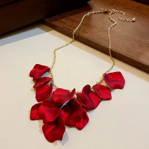Détail d'un collier chaîne dorée avec pétales de fleurs rouges sur surface neutre.