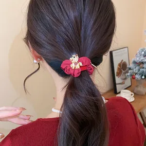 Chouchou rouge élégant avec breloque cheval dorée porté sur une queue de cheval chic.