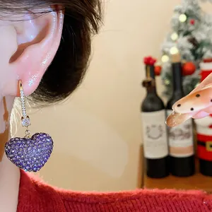 Close-up of a purple heart-shaped earring with pavé zircon crystals on a gold hook