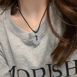 Close-up of a white jade Pingan Kou pendant necklace worn on a gray T-shirt