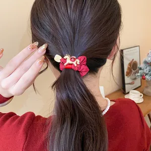 Détail d'un chouchou rouge avec un charme de cheval doré porté dans une coiffure en queue de cheval