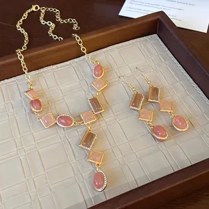 Close-up of vintage geometric necklace and earrings with peach stones in a wooden tray.